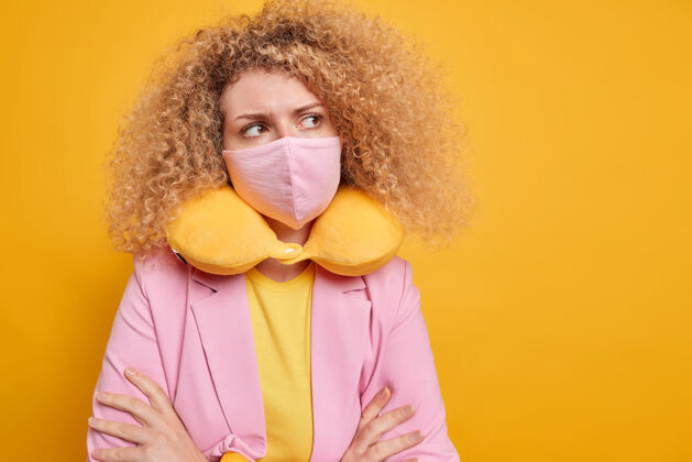 脸体贴的女人正在自我隔离戴着防冠状病毒的防护面具戴着颈枕双臂合十沉思着隔离在黄色墙壁上的东西Quarantine安全空白