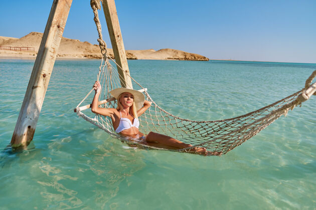 度假村旅行和度假的概念妇女放松吊床在海上海洋比基尼女人