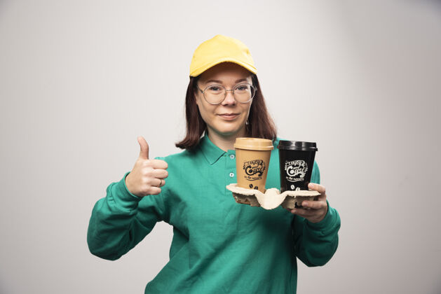 美味一位女送货员举着大拇指 手里拿着一张白色的纸板咖啡杯高质量的照片送货性感年轻人