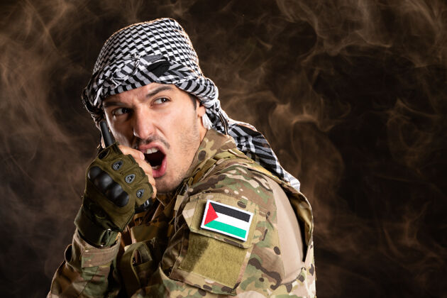 枪一名巴勒斯坦士兵在黑暗的墙上通过无线电台讲话成人男性制服