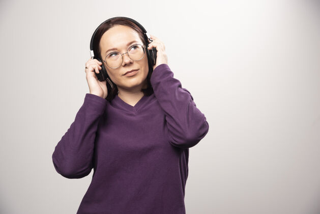 人类戴着眼镜的年轻女子戴着耳机在听音乐 这是一张高质量的白色照片青春模特年轻