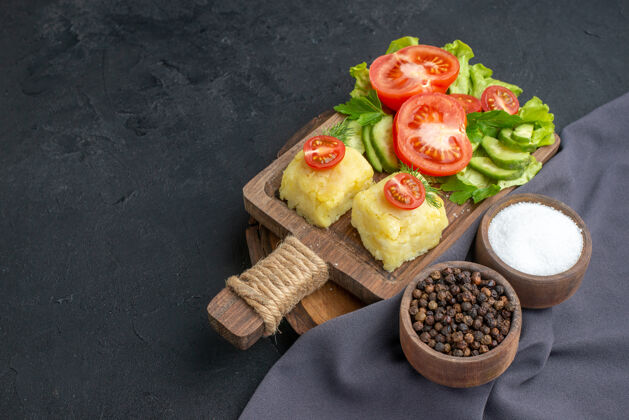 健康切碎的新鲜蔬菜正面图切菜板上的奶酪和黑色表面上深色毛巾上的香料奶酪番茄午餐