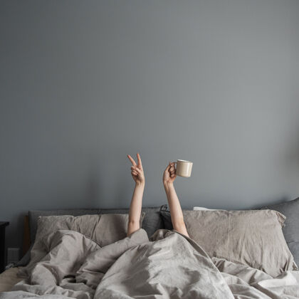 咖啡女人躺在床上 手里拿着咖啡杯 展示胜利的象征茶极简主义女孩