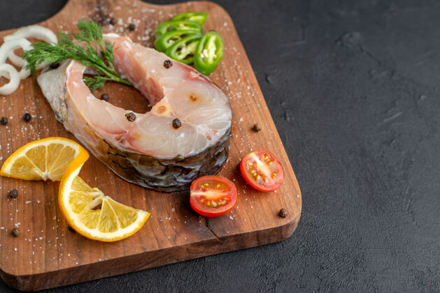 生鱼特写镜头的生鱼和新鲜切碎的蔬菜柠檬片香料在一个木板上右侧的黑色苦恼的表面食物切片上