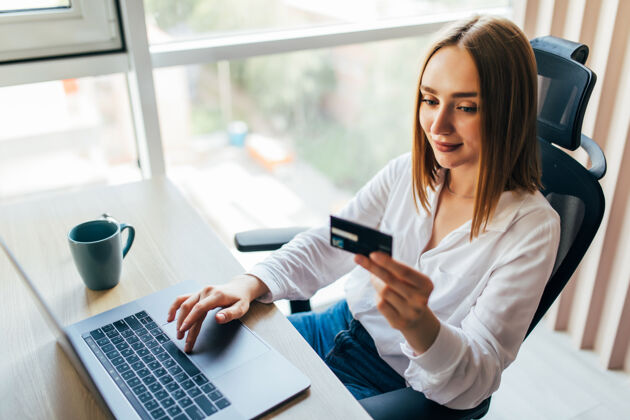 家庭购物一个女人拿着信用卡在家里使用笔记本电脑的肖像网上购物销售电子银行