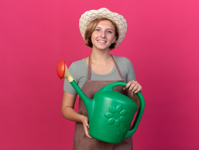 园艺微笑的年轻斯拉夫女园丁戴着园艺帽拿着浇水罐斯拉夫戴粉色