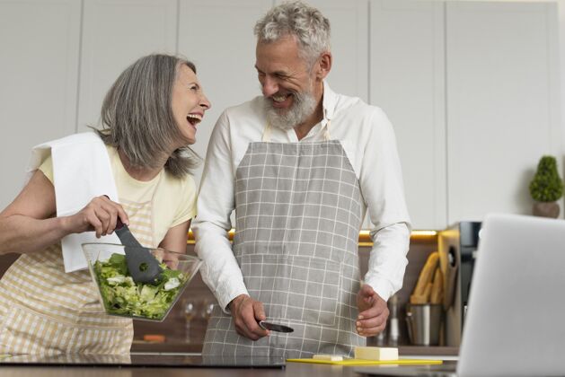 围裙老两口在厨房用笔记本电脑上烹饪课女性学习丈夫