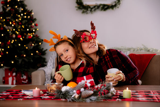 桌子高兴的母女俩捧着杯子坐在餐桌旁 在家里享受圣诞时光请享受时间女儿