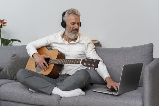 老年人老人在家的沙发上用笔记本电脑学习吉他课内部原声吉他室内