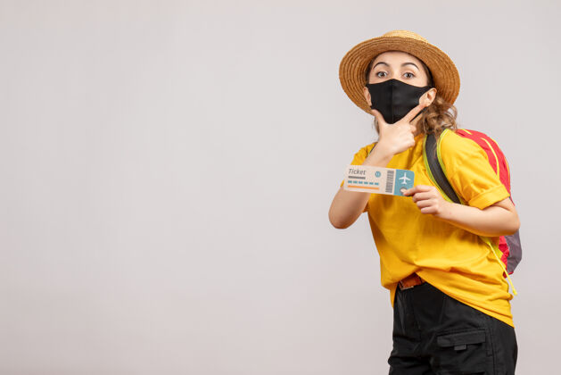 票正面图：戴着黑色面具的年轻女子拿着旅行票 手放在下巴上旅游乐趣旅游