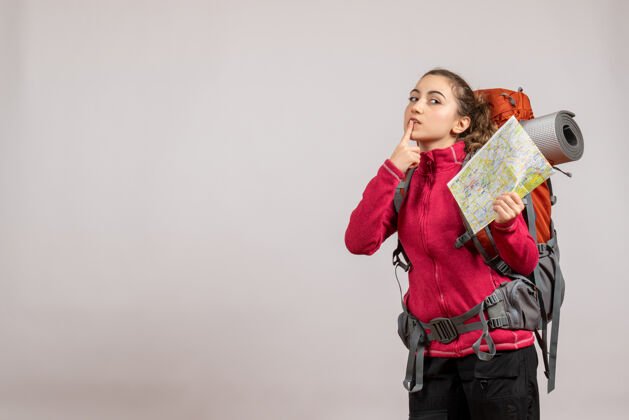 手指正面图：年轻的旅行者 背着大背包 举着地图 手指放在嘴上旅行者年轻的旅行者向上