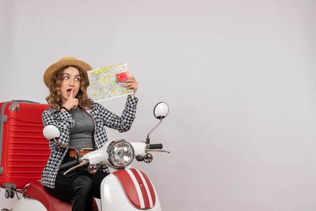 年轻女子前视图：骑着轻便摩托车的年轻女子拿着卡片和地图地图信用卡人