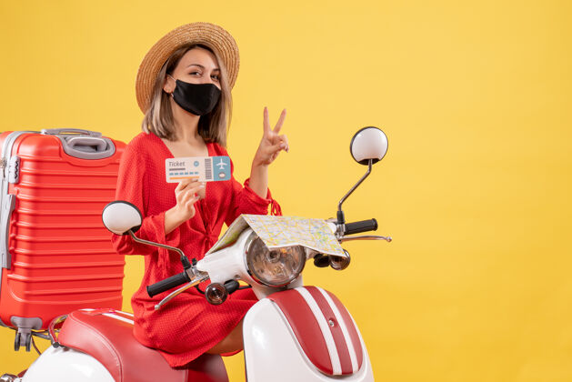 冒险正面图：戴着黑色面罩的年轻女士 骑着轻便摩托车 提着红色手提箱 拿着票子 示意胜利标志旅行者票面罩