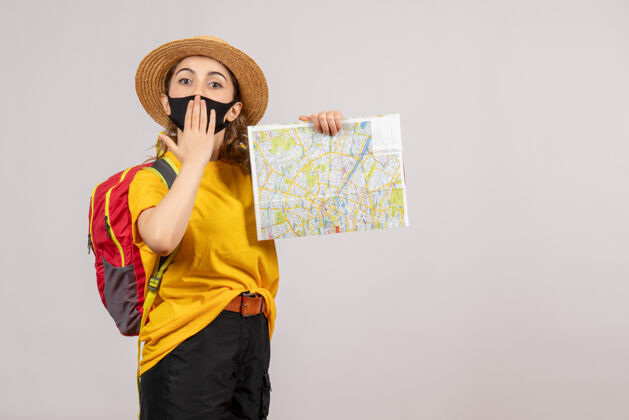 成人正面图：年轻的旅行者背着背包 把地图放在嘴边手灰色背包