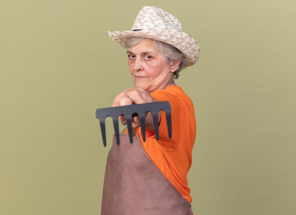 园艺高兴的上了年纪的女园丁戴着园艺帽站在一旁伸出耙子绿色请老人