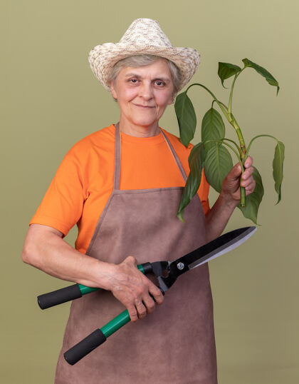 女高兴的上了年纪的女园丁戴着园艺帽手持园艺剪刀和花枝树枝园艺请