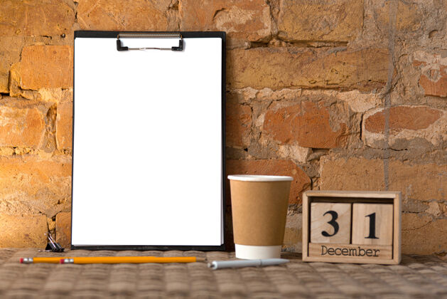 剪辑棕色砖墙上的空白剪贴板上有咖啡杯和铅笔复印空间 12月31日 新年决议信息空白手机