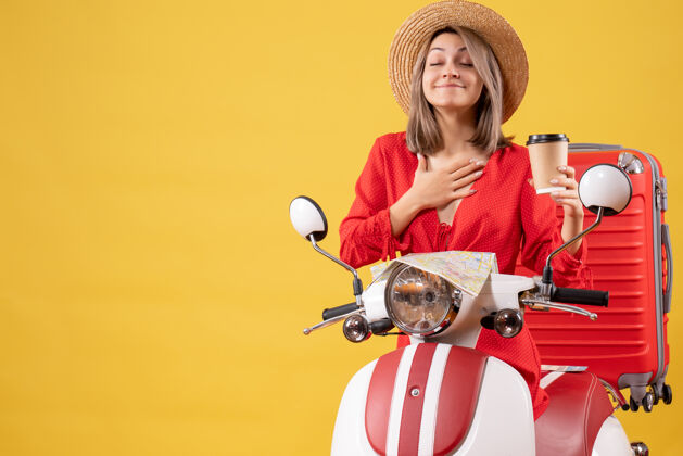 旅游正面图身穿红色连衣裙的年轻女士闭上眼睛拿着咖啡杯靠近轻便摩托车度假可爱轻便摩托车
