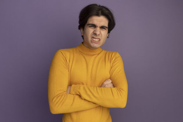 衣服皱眉的年轻帅哥穿着黄色高领毛衣双手交叉隔离在紫色的墙上手高领毛衣脸