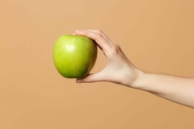 手臂近距离拍摄的女性手里拿着新鲜成熟的青苹果 隔离在米色粉彩墙上新鲜食物苹果