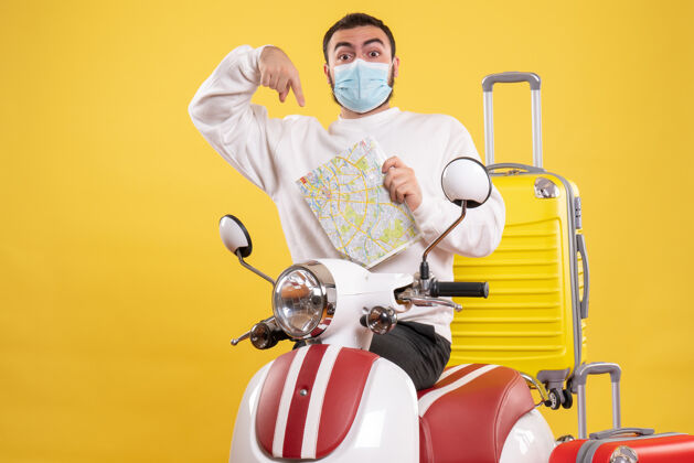 顶部旅行概念的俯视图 戴着医用面罩的年轻人站在黄色手提箱的摩托车旁黄色人摩托车