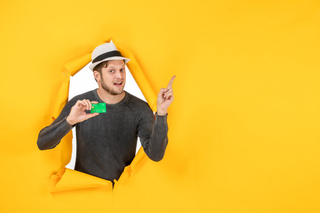 帽子顶视图微笑的家伙拿着银行卡 指着撕破的黄色墙壁微笑的家伙帽子指向