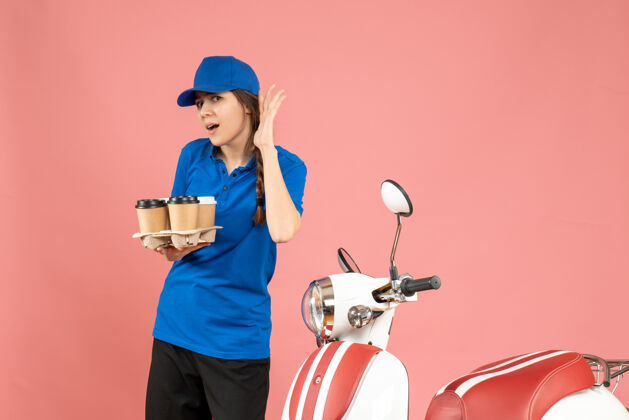 工人前视图：信使女孩站在摩托车旁 手里拿着咖啡和小蛋糕 在柔和的桃色背景下听着最后的闲话小工作粉彩
