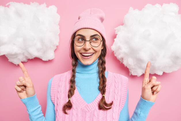 眼镜在白云上点着辫子的女孩展示着什么 戴着帽子 高领圆领眼镜 穿着粉红色的背心辫子舒适帽子