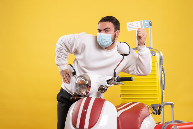 年轻人旅行概念的俯视图 戴着医用面罩的年轻人站在摩托车旁边 黄色手提箱在上面 手里拿着车票人微笑持有