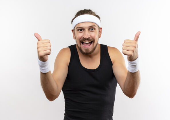穿快乐的年轻英俊的运动型男子戴着头带和腕带 竖起大拇指孤立在白墙上男人运动腕带