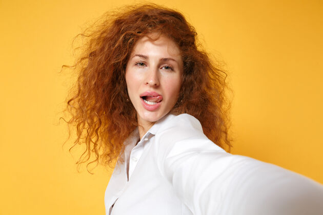 女性性感的年轻红发女女孩在白色衬衫的特写镜头摆在黄色橙色的墙上孤立秀肖像时尚