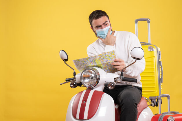 旅行旅行的概念与思维的家伙在医疗面具坐在摩托车上黄色手提箱上 并显示黄色地图手提箱吉他黄色