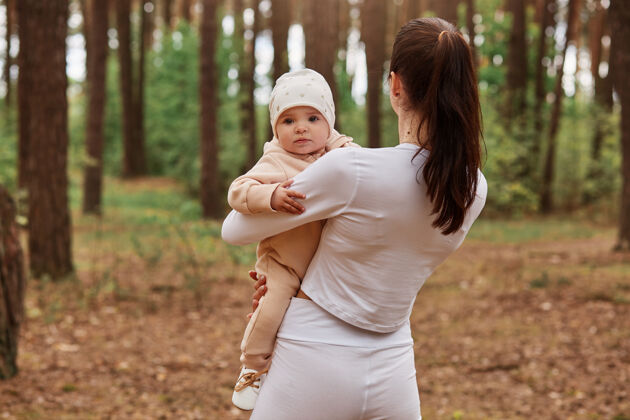 自然后视图：苗条的女人站在树林中 手里抱着婴儿 孩子看着前面树爱婴儿