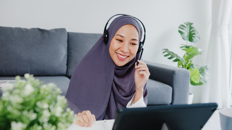 沙发女士戴着耳机用平板电脑在客厅工作时通过电话会议和同事谈论销售报告年轻人妇女女性