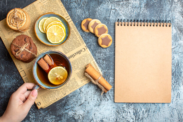 手捧的上图是美味的饼干和手拿着一杯红茶与肉桂放在一张旧报纸上旧的背景笔记本