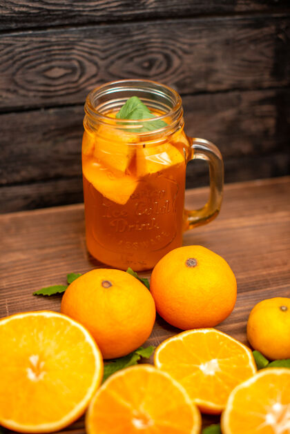 自然前视图的整体和切鲜橙子与叶子和天然果汁在一个杯子在一个棕色的背景前面果汁叶子