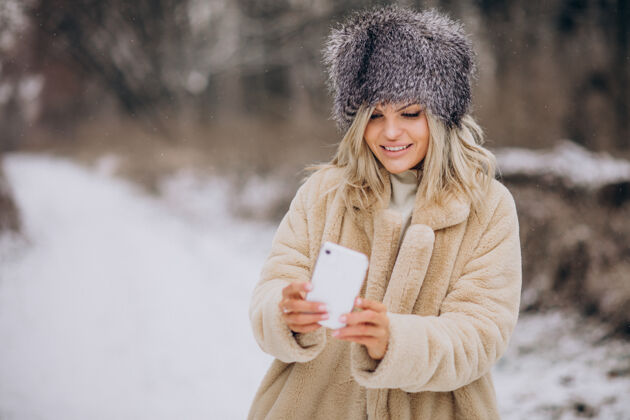 女性穿着冬衣的女人走在满是雪的公园里打电话寒冷降雪探索