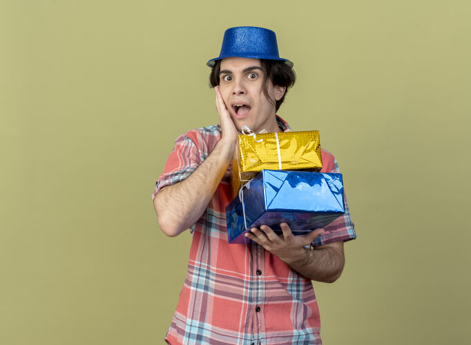 帽子戴着蓝色派对帽的白人帅哥惊讶地把手放在脸上 手里拿着礼盒空间盒子举行
