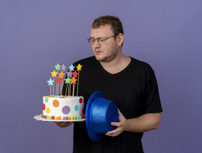 蓝色笨手笨脚的成年斯拉夫人戴着眼镜 手里拿着蓝色的派对帽和生日蛋糕空间举行眼镜