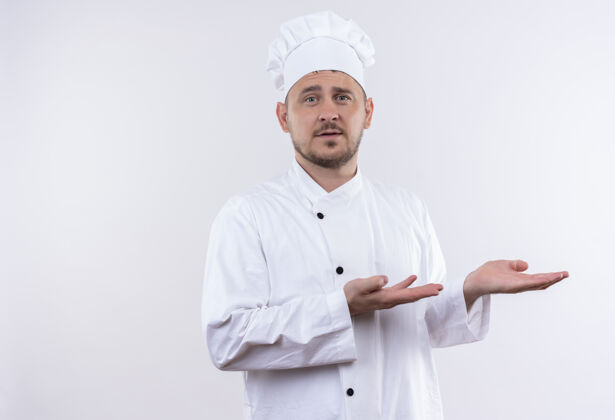 印象年轻帅气的厨师身着厨师制服 双手指着隔离在白墙上的一侧手帅烹饪