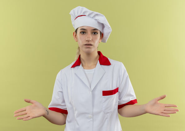 印象令人印象深刻的年轻漂亮厨师在厨师制服显示空手孤立在绿墙上手厨师年轻