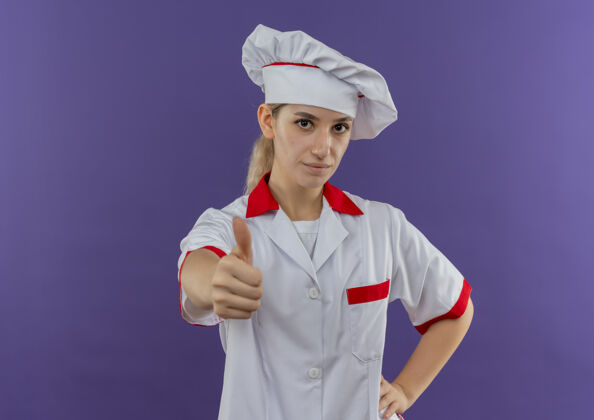 腰围自信的年轻漂亮厨师 身着厨师制服 手放在腰上 大拇指竖立在紫色的墙上 留有复制空间烹饪自信手