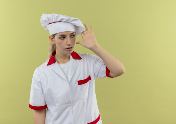 年轻年轻漂亮的厨师穿着厨师制服看着侧面把手放在头附近看着侧面隔离在绿色墙上的复制空间手印象头