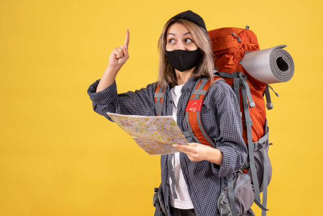 背包带着黑色面具和背包的旅行女孩拿着地图 手指朝上地图人成人