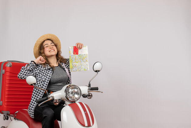 摩托车喜出望外的年轻女子骑着轻便摩托车 手里拿着灰色的卡片和地图灰色肖像人