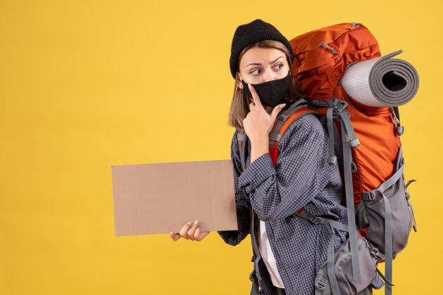 面具旅行女孩带着黑色的面具和背包拿着纸板看着右边女旅行者成人肖像