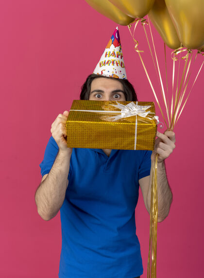 生日帅气的白种人戴着生日帽手持氦气球和礼盒复制空间穿