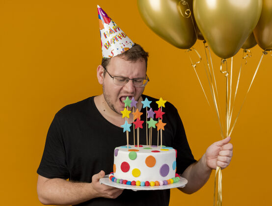 蛋糕一个戴着光学眼镜 戴着生日帽 手持氦气球和生日蛋糕的未获释的成年斯拉夫男子氦生日帽子