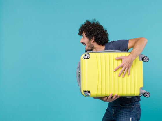举行度假的男人拿着蓝色的大黄色手提箱蓝色大乐趣