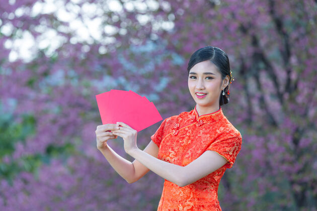 欢呼美丽的亚洲女人在中国的新年里展示一些东西和拿红包红色衣服女孩